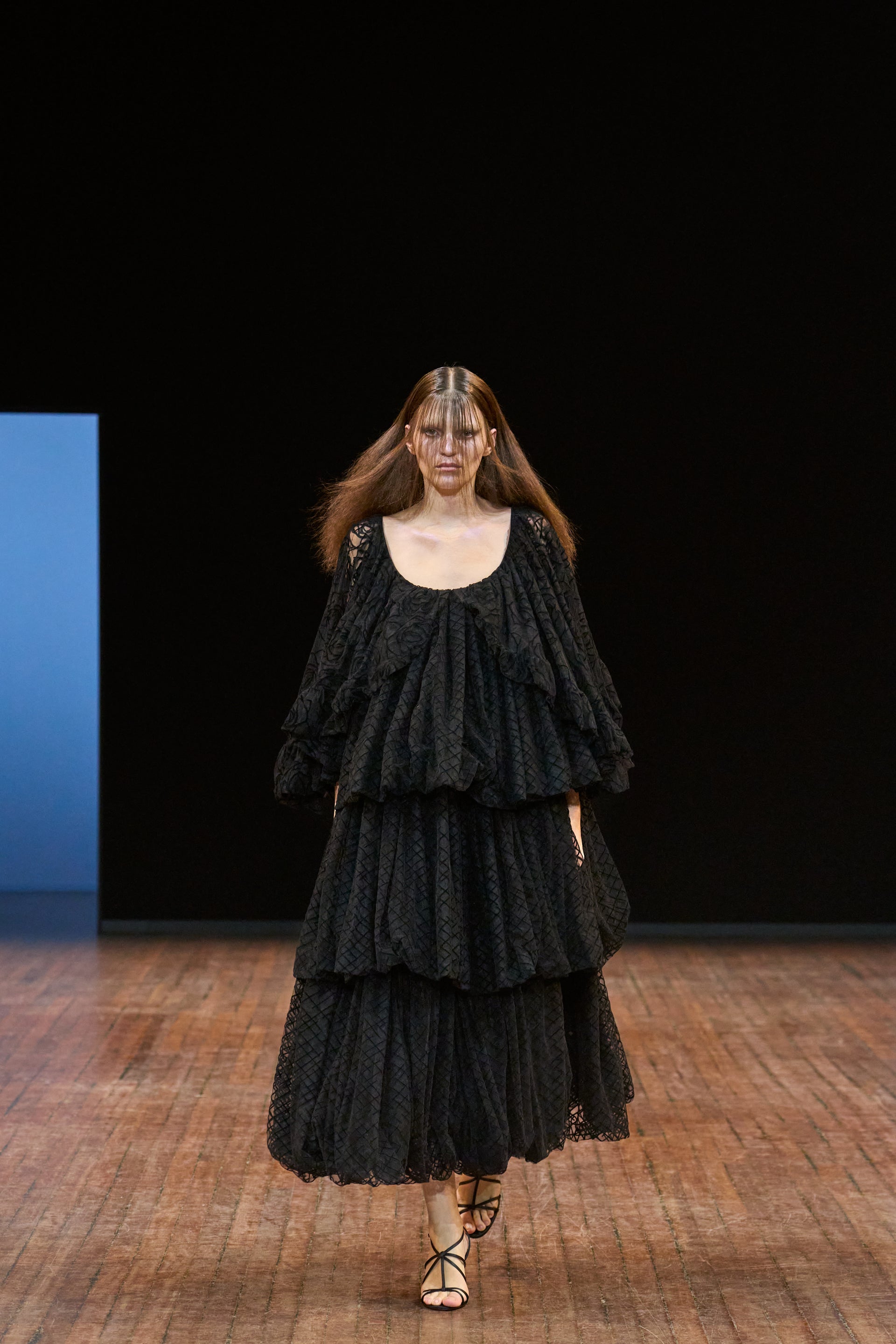 Model wearing a black layered dress on a runway with a dark background