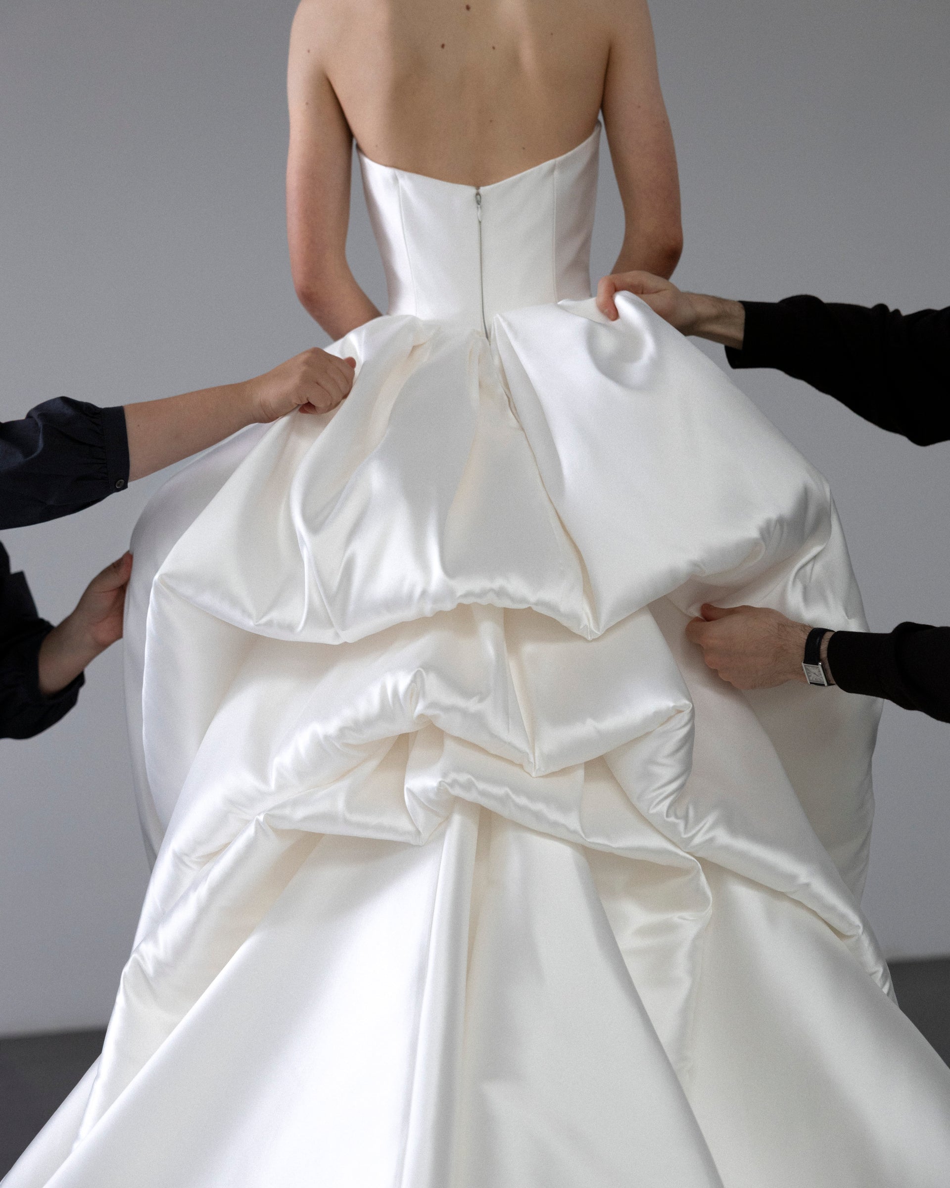 White wedding dress with a large bow being adjusted by hands against a neutral background