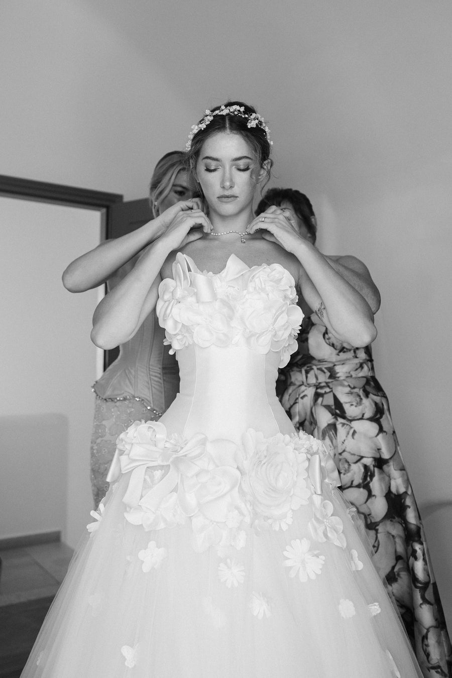 Bride getting ready with assistance, wearing a floral headpiece and gown.