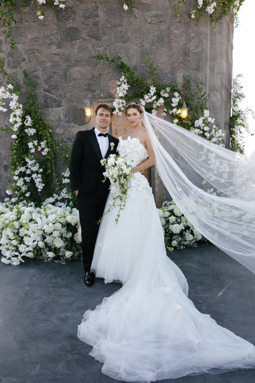 Wedding couple standing in front of a stone wall with floral decorations.