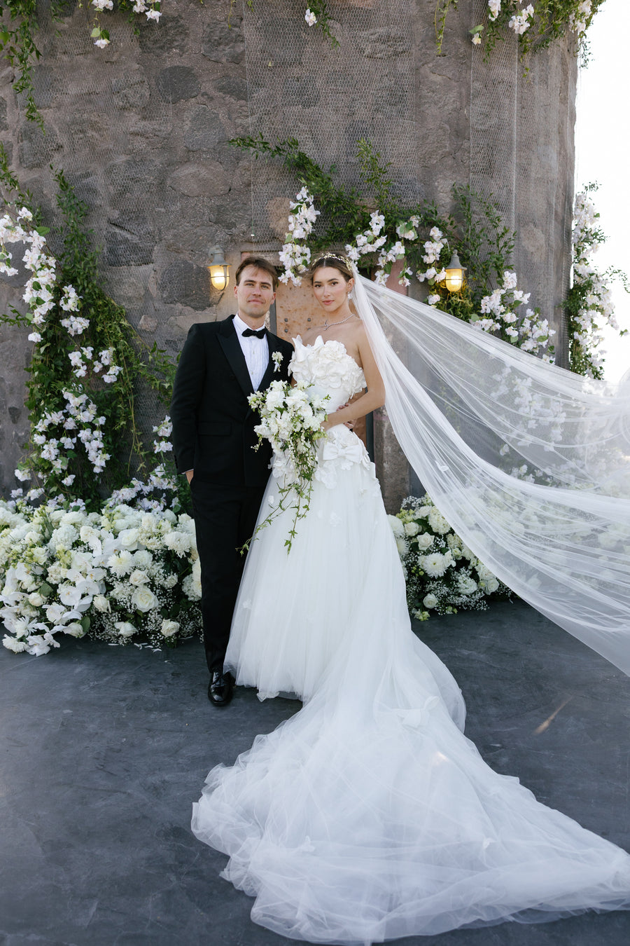 Wedding couple standing in front of a stone wall with floral decorations.
