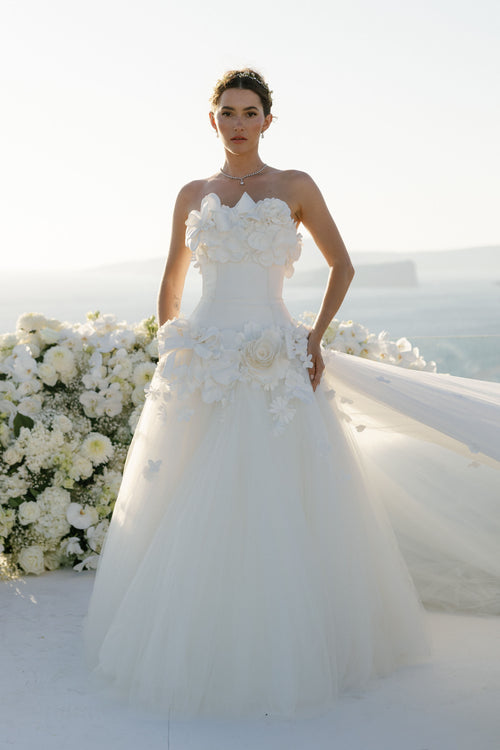 Woman in a white wedding dress with floral details standing against a white background