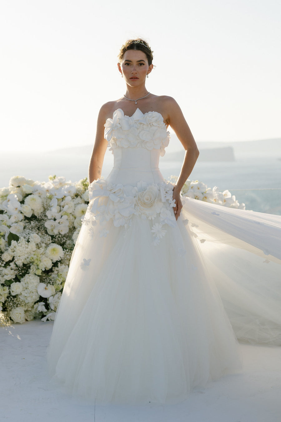 Woman in a white wedding dress with floral details standing against a white background
