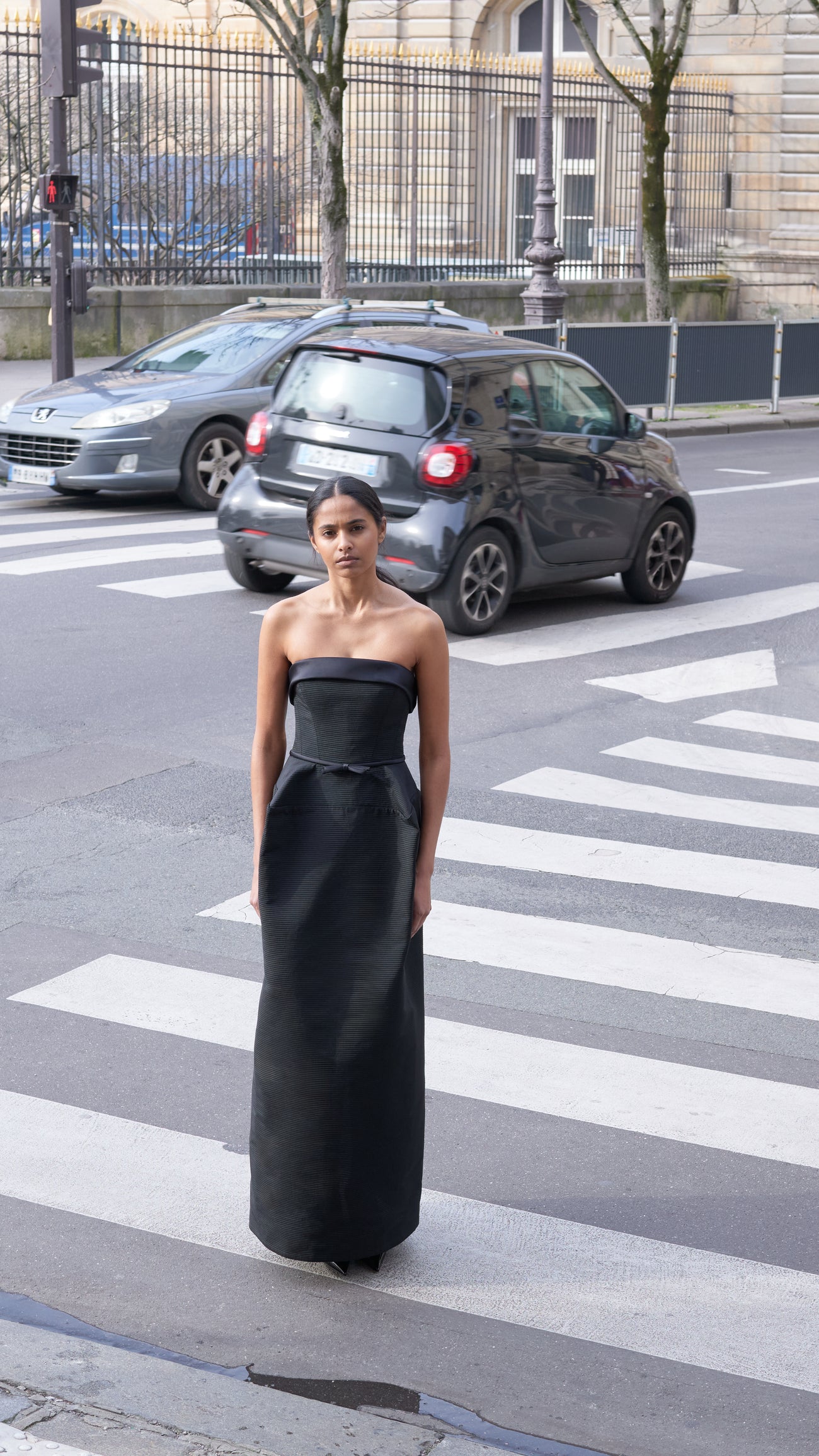 Model standing outside on a busy street wearing a long black gown.