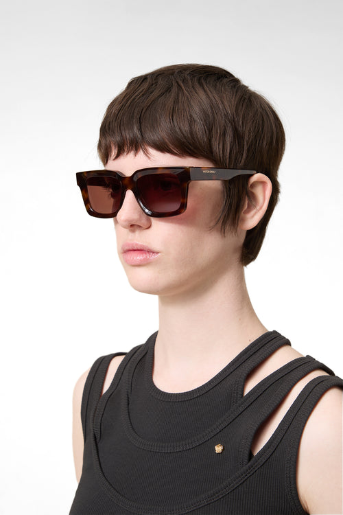 Model wearing square tortoise glasses on a white background.