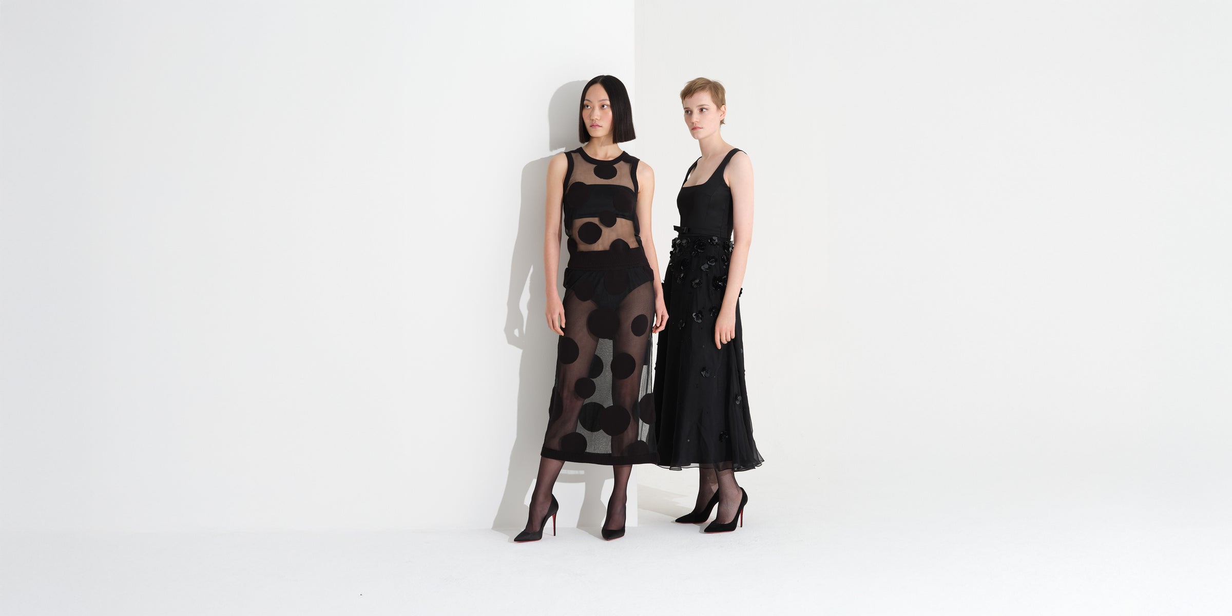 Two models on white background wearing black polkadot dress and floral embroidery dress. 