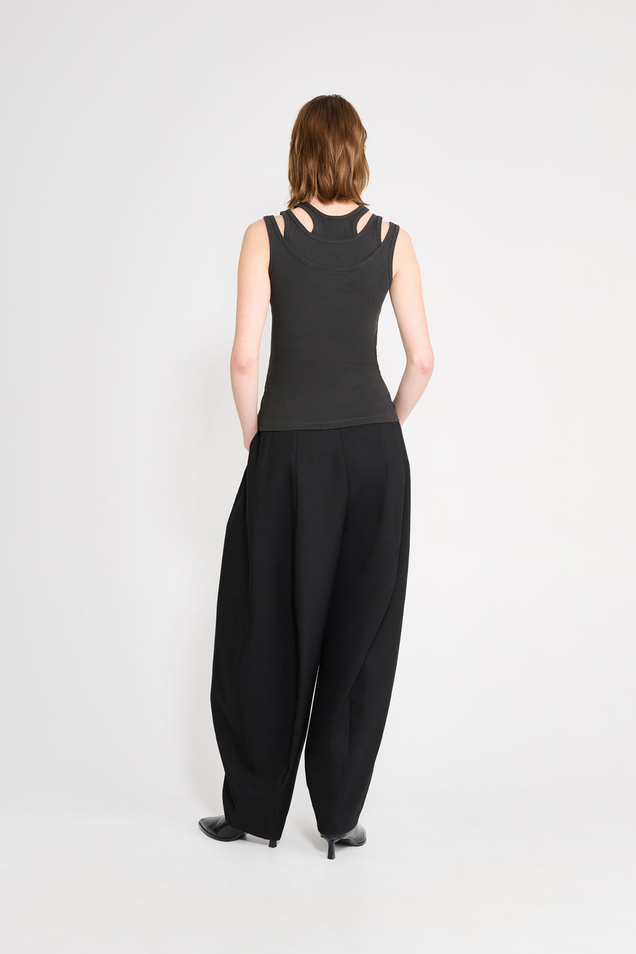 Person wearing a black sleeveless top and wide-leg pants on a white background