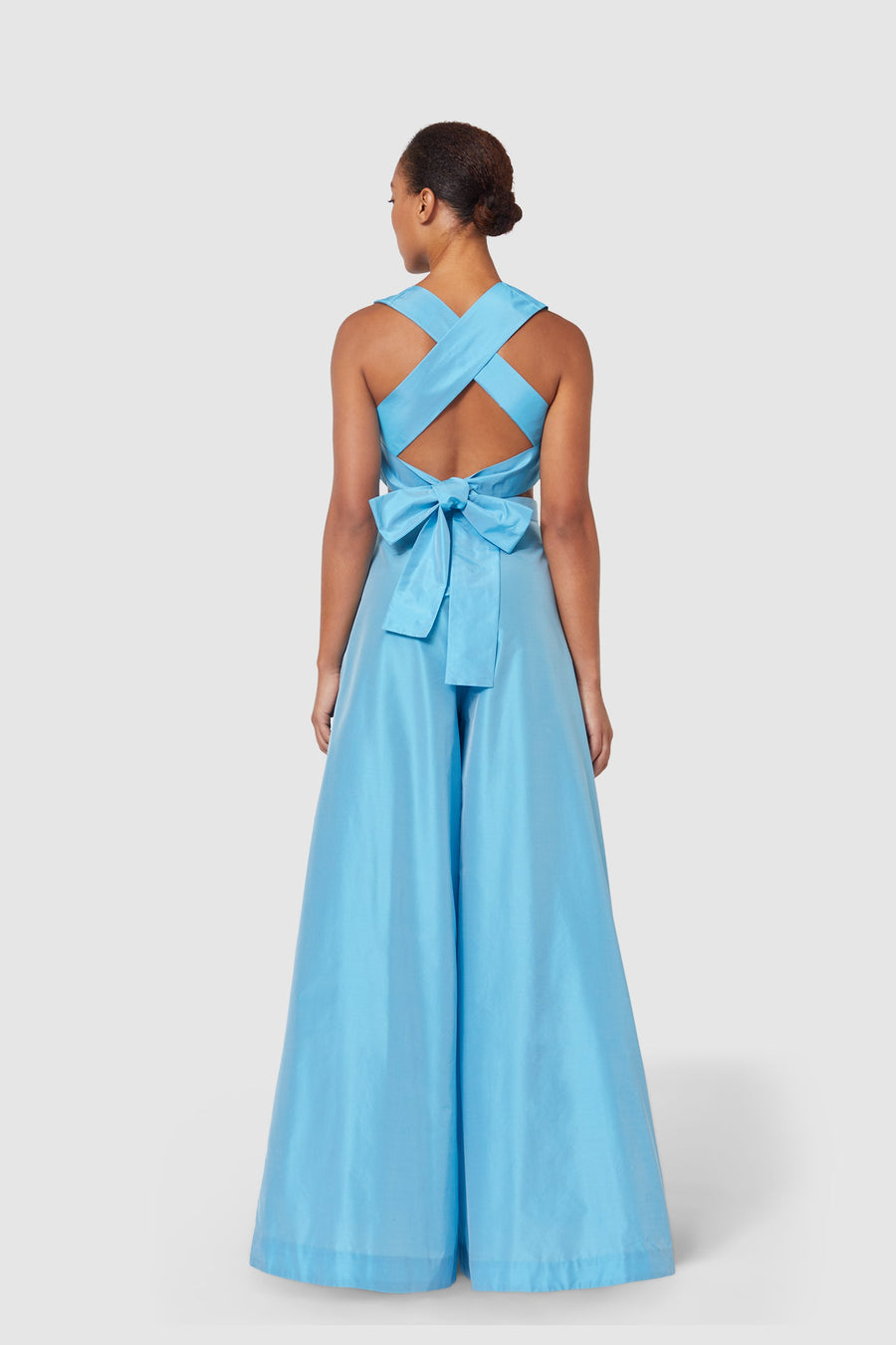Back view of a cobalt blue satin jumpsuit featuring a crisscross halter neckline and an oversized bow detail at the waist.