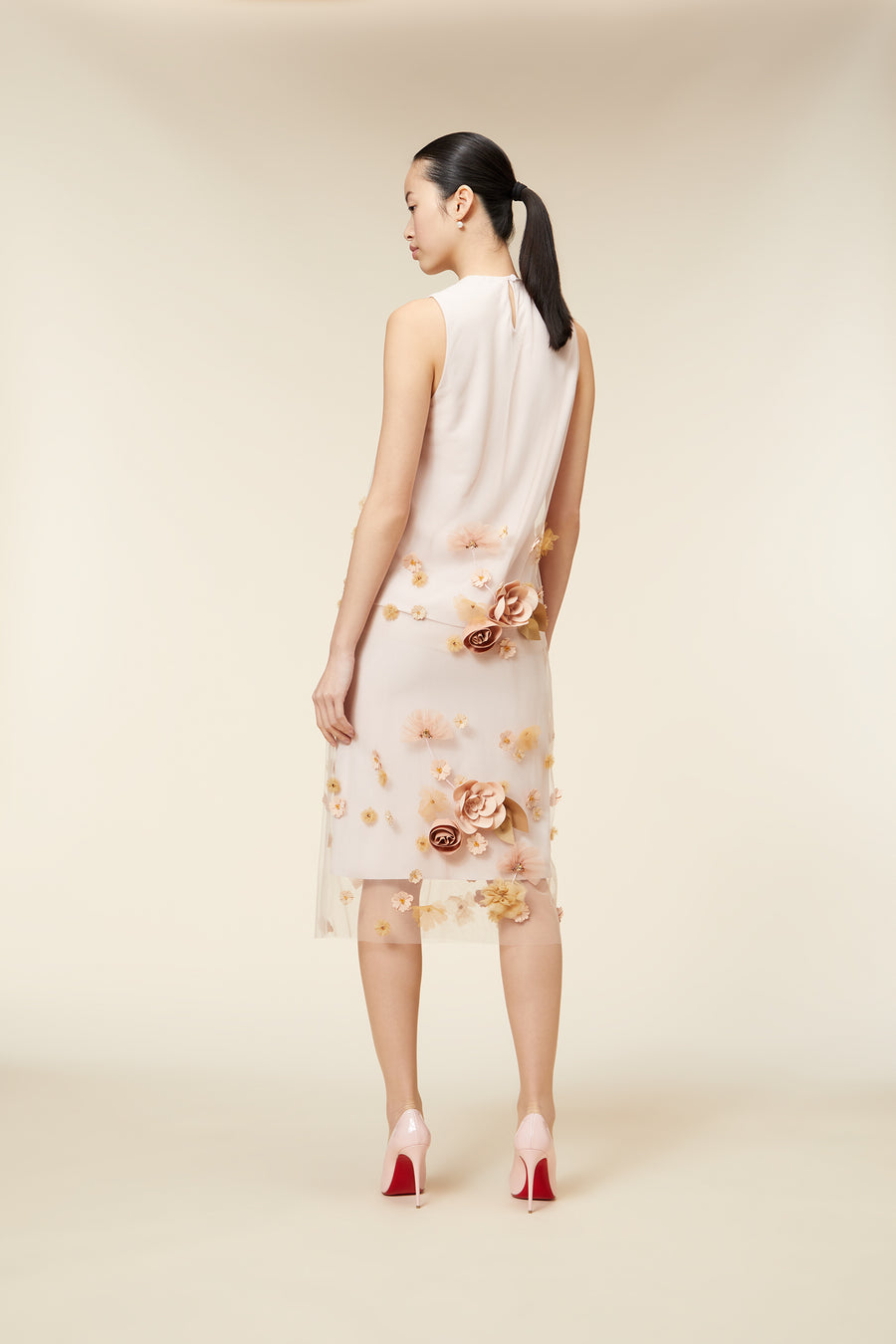 A sleeveless dress features delicate floral applique over a sheer base, paired with elegant pink high heels.