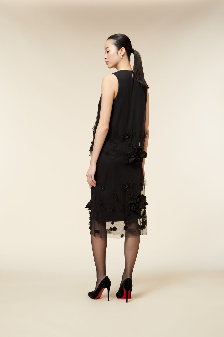 Elegant black dress with intricate floral appliques and sheer overlay, paired with classic black stilettos featuring red soles.