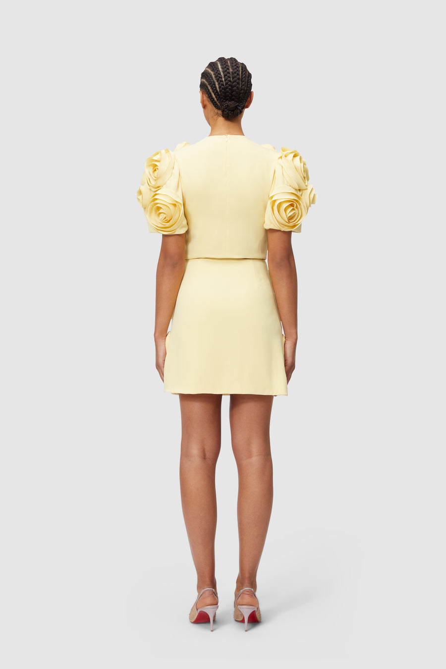 Yellow dress with structured, rose-embellished puff sleeves creates a striking silhouette, paired with elegant heels.