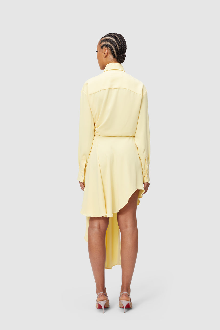 Yellow asymmetrical dress with long sleeves and soft drape detail, paired with elegant silver high-heeled sandals.