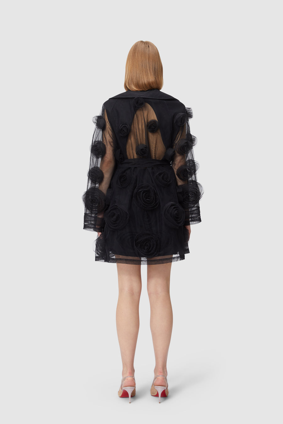 Black sheer dress adorned with large tulle floral accents, featuring an open back design, paired with pink-heeled sandals.