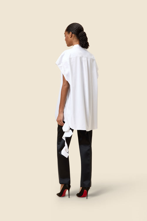Model in a sleek white oversized blouse with side ribbons paired with black trousers and stylish red-soled heels.