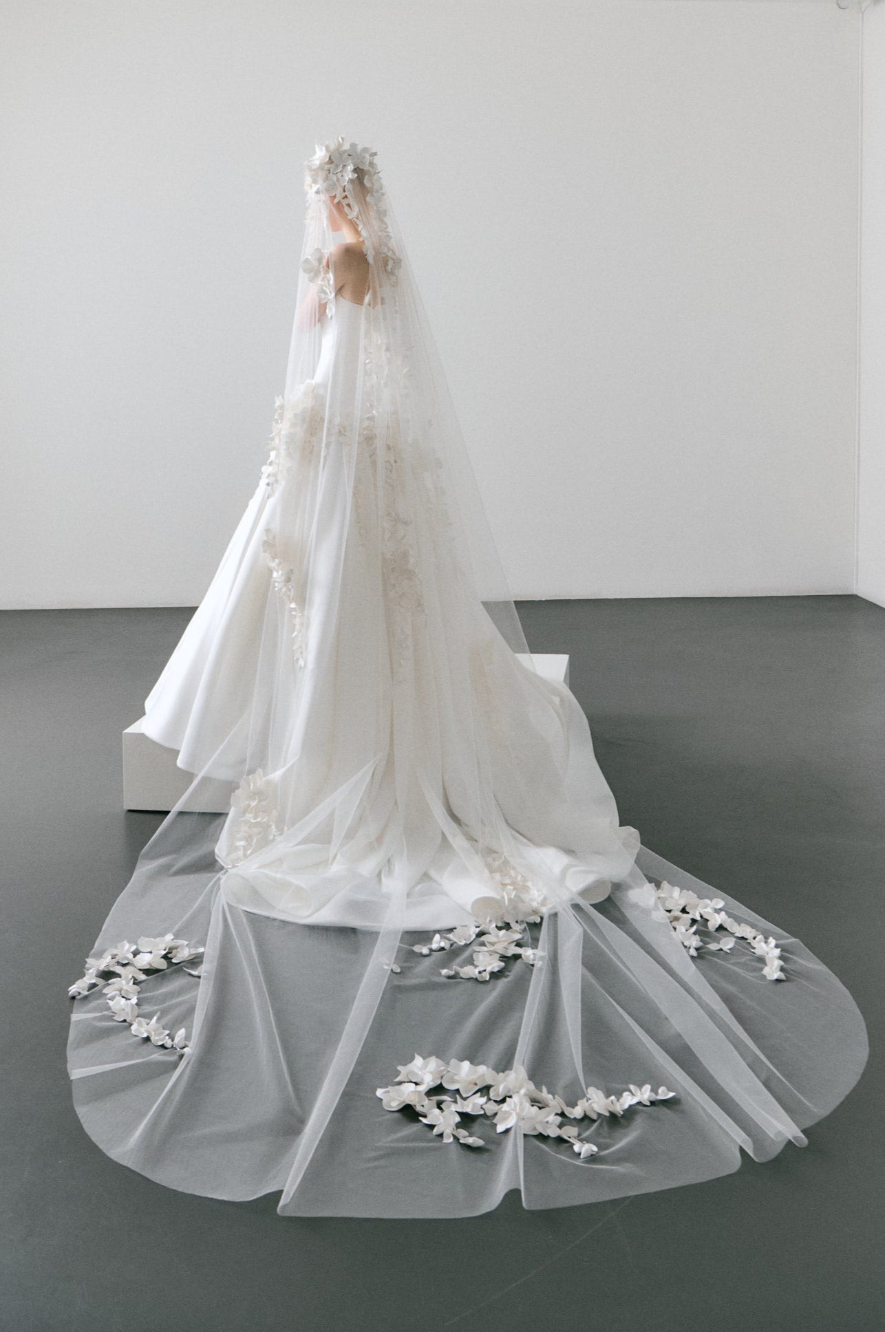 White wedding dress with floral details on a mannequin in a minimalistic room.
