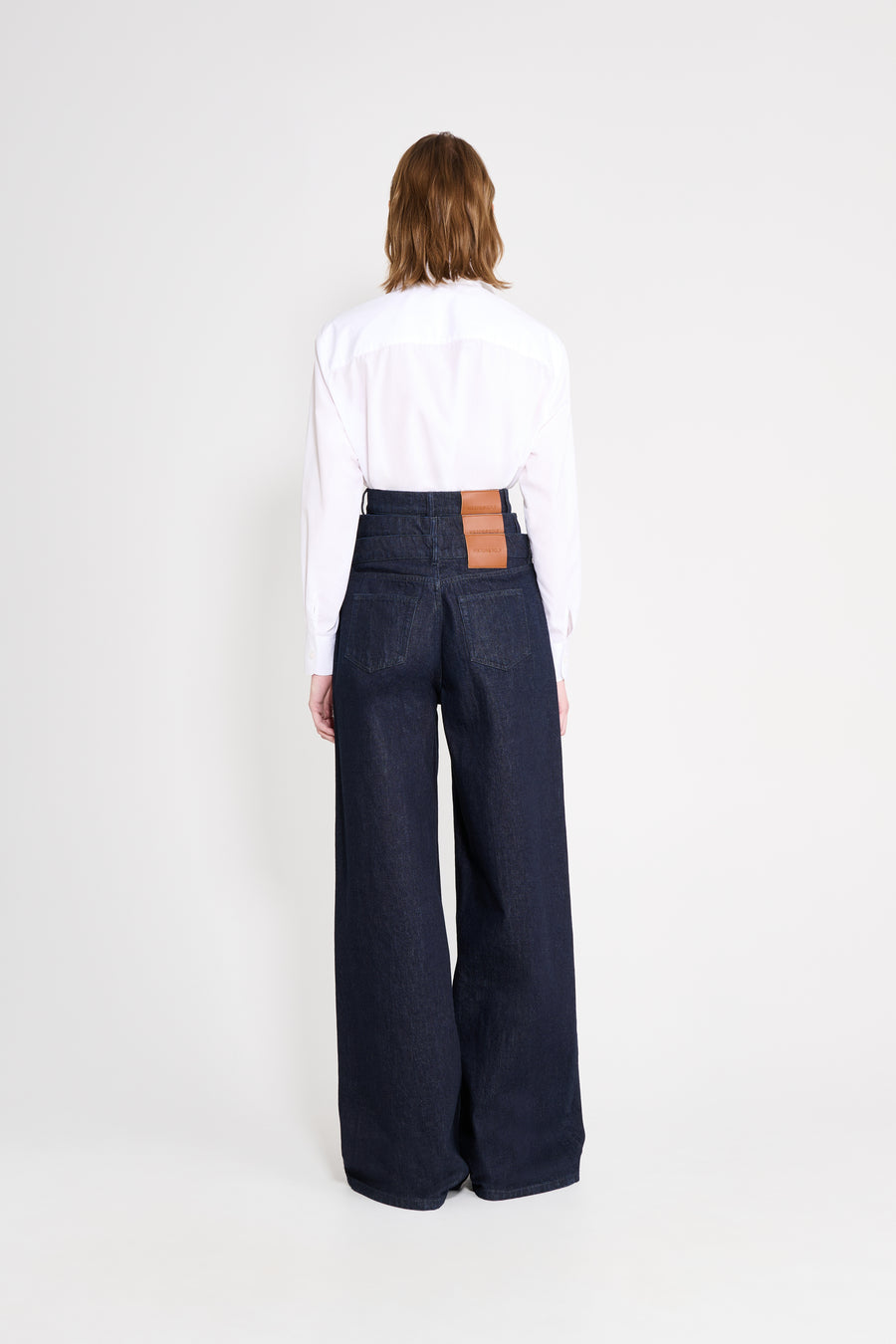 Person wearing a white shirt and dark blue wide-leg jeans with a brown patch on a white background