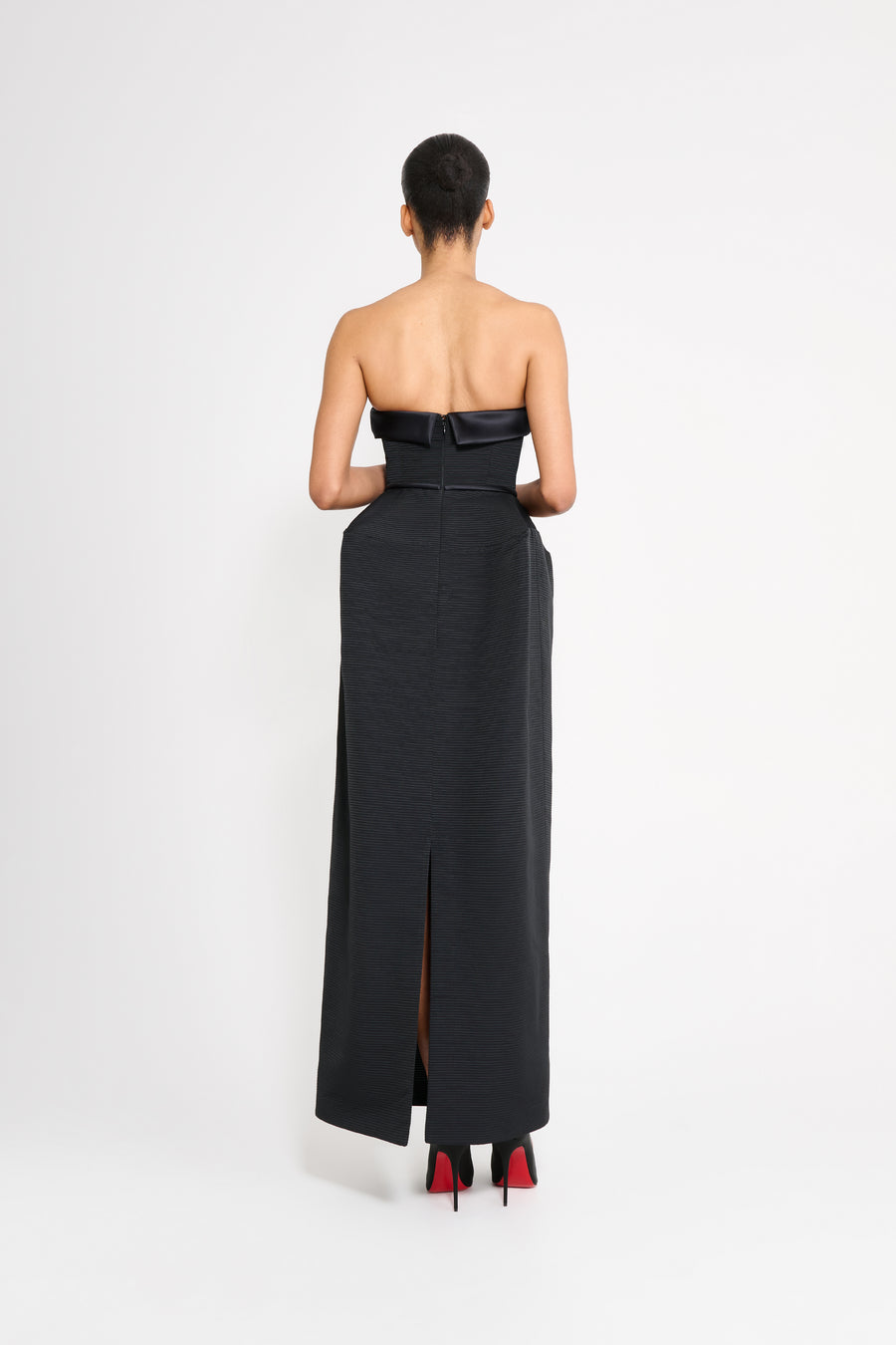 Woman wearing a black strapless gown with a slit on a white background