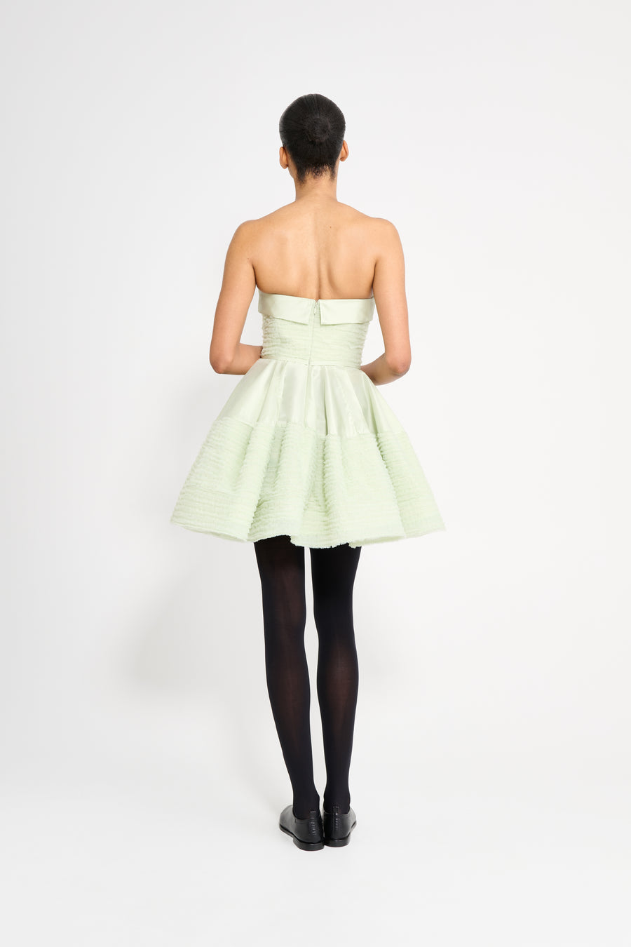 Woman wearing a light green strapless dress on a white background