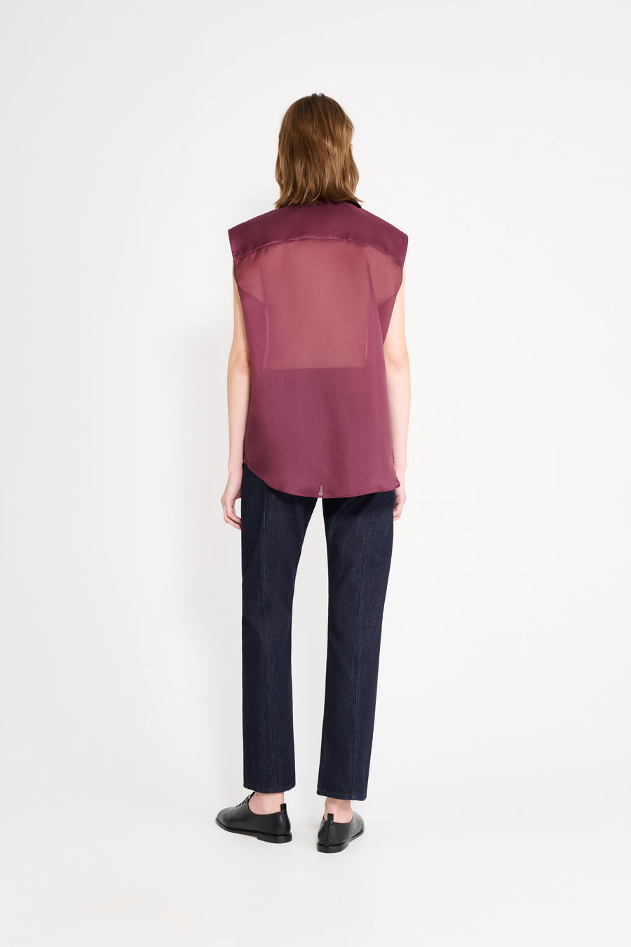 Person wearing a sheer burgundy top and dark pants on a white background