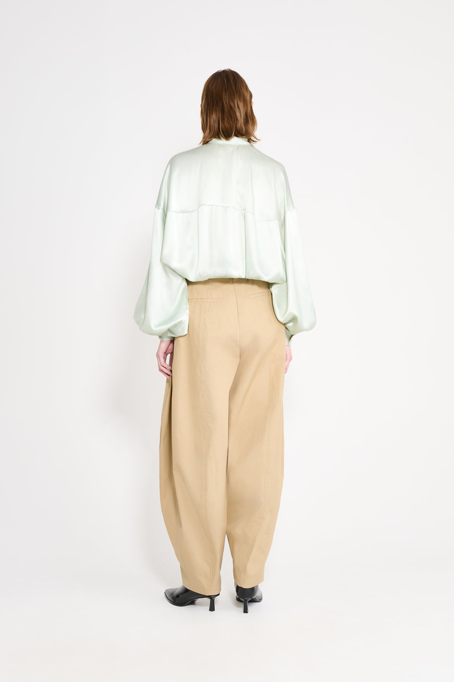 Person wearing a mint blouse and beige pants on a white background