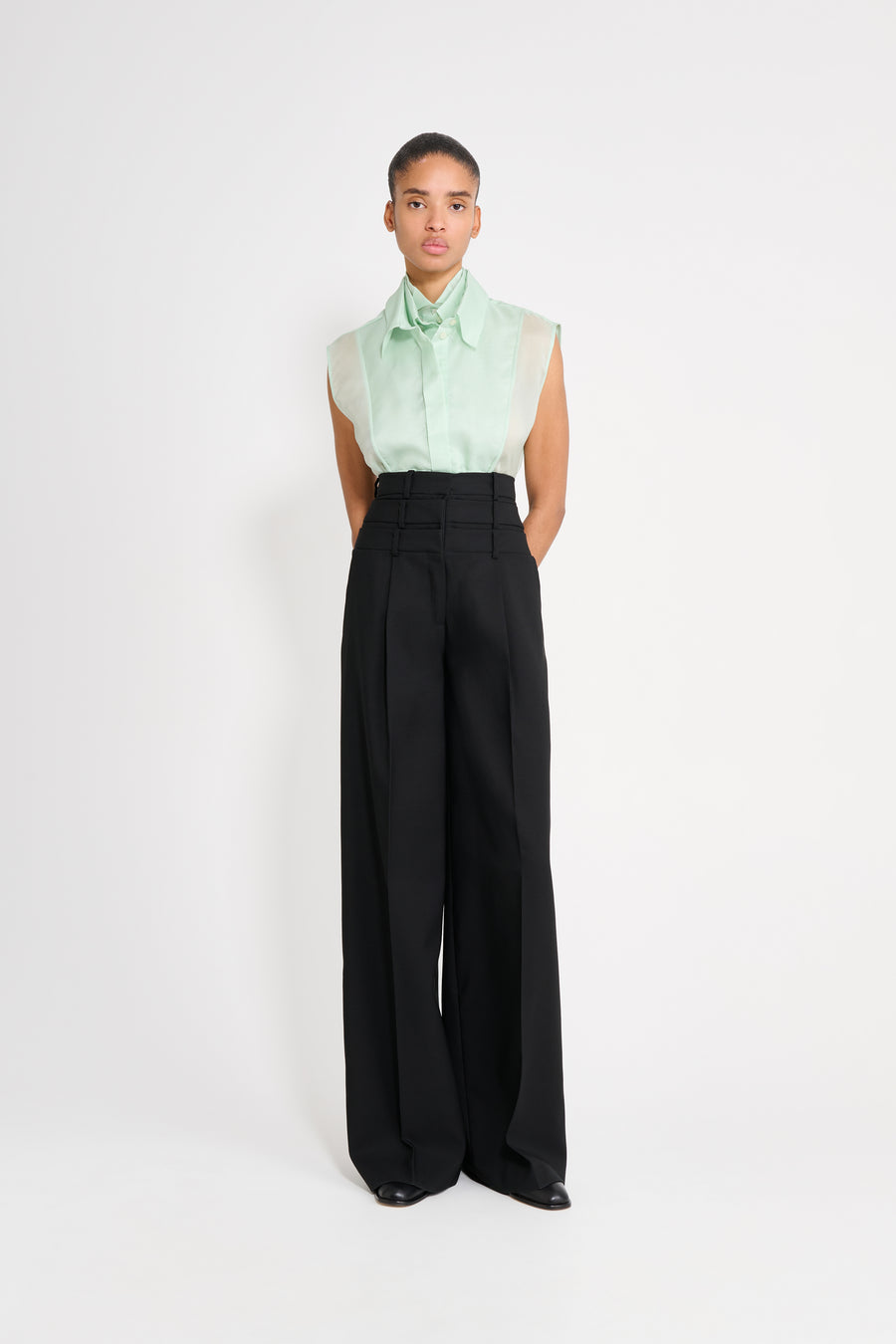 Person wearing a light green blouse and black pants on a white background