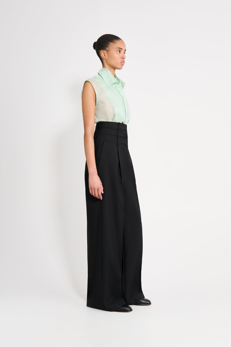 Woman wearing a light green sleeveless top and black wide-leg pants on a white background