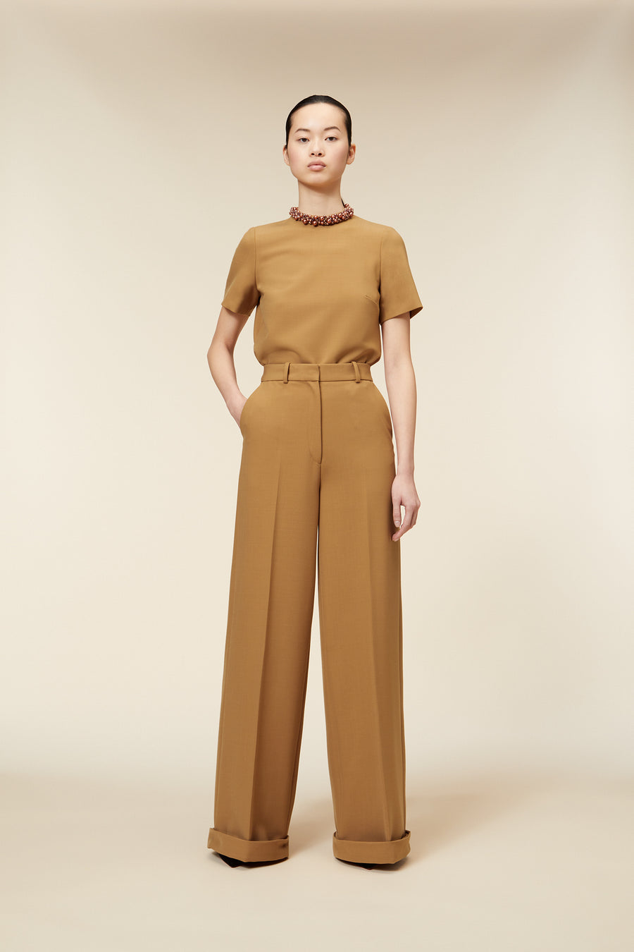 Tailored camel wool high-waisted trousers paired with a matching short-sleeved top, accessorized with a beaded necklace.