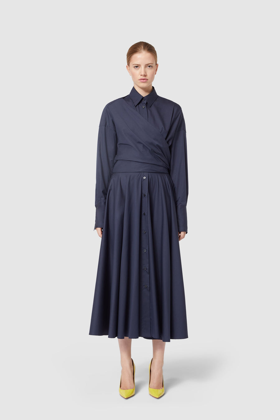 Elegant navy cotton wrap dress features long sleeves and a button-down A-line skirt, complemented by vibrant yellow heels.