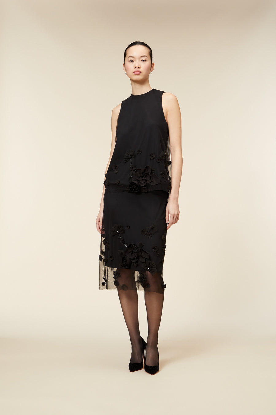 Black floral embroidered gown with sheer hem detailing, showcasing elegant 3D flower appliqués and refined sleeveless design.