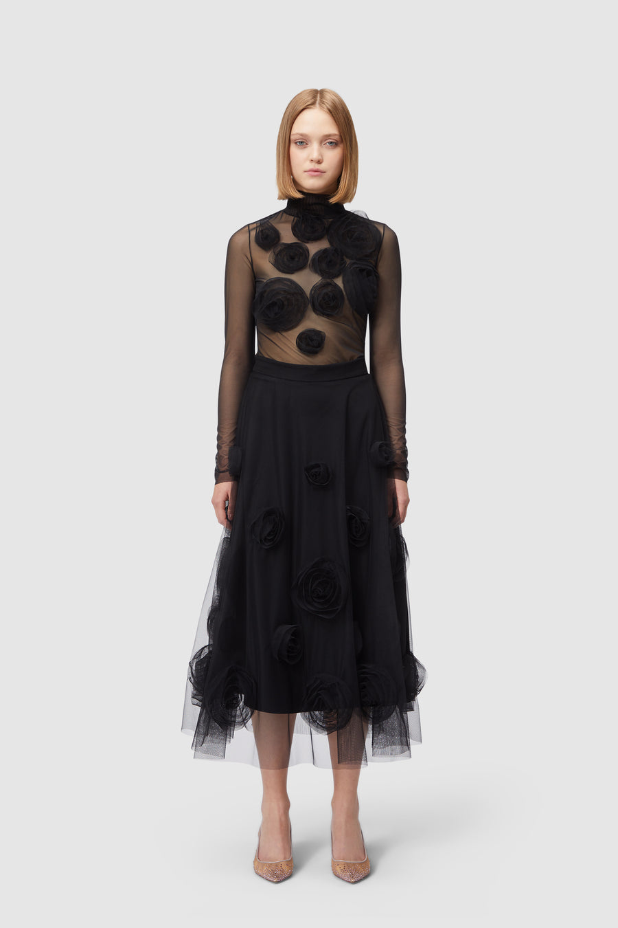 Elegant dress with sheer long sleeves adorned with large black floral appliqués over a full tulle skirt.
