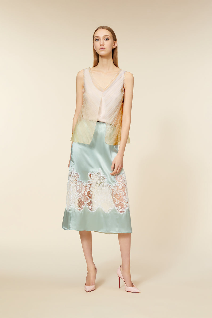 A model wearing a pastel tulle top with a light blue satin skirt featuring intricate lace detailing, paired with pink heels.