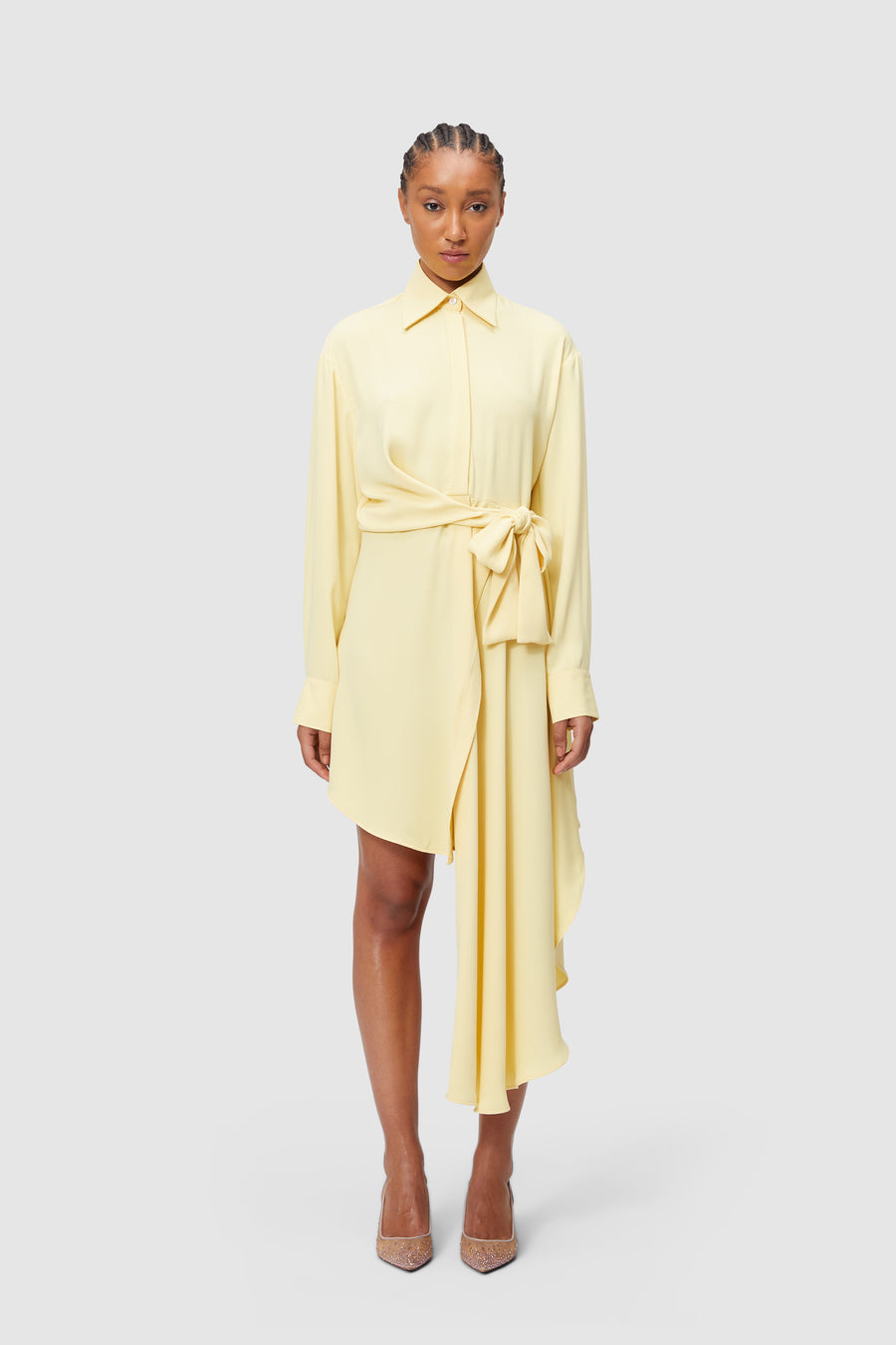 A pale yellow shirt dress with an asymmetric hem and waist tie, featuring a classic collar and long sleeves.