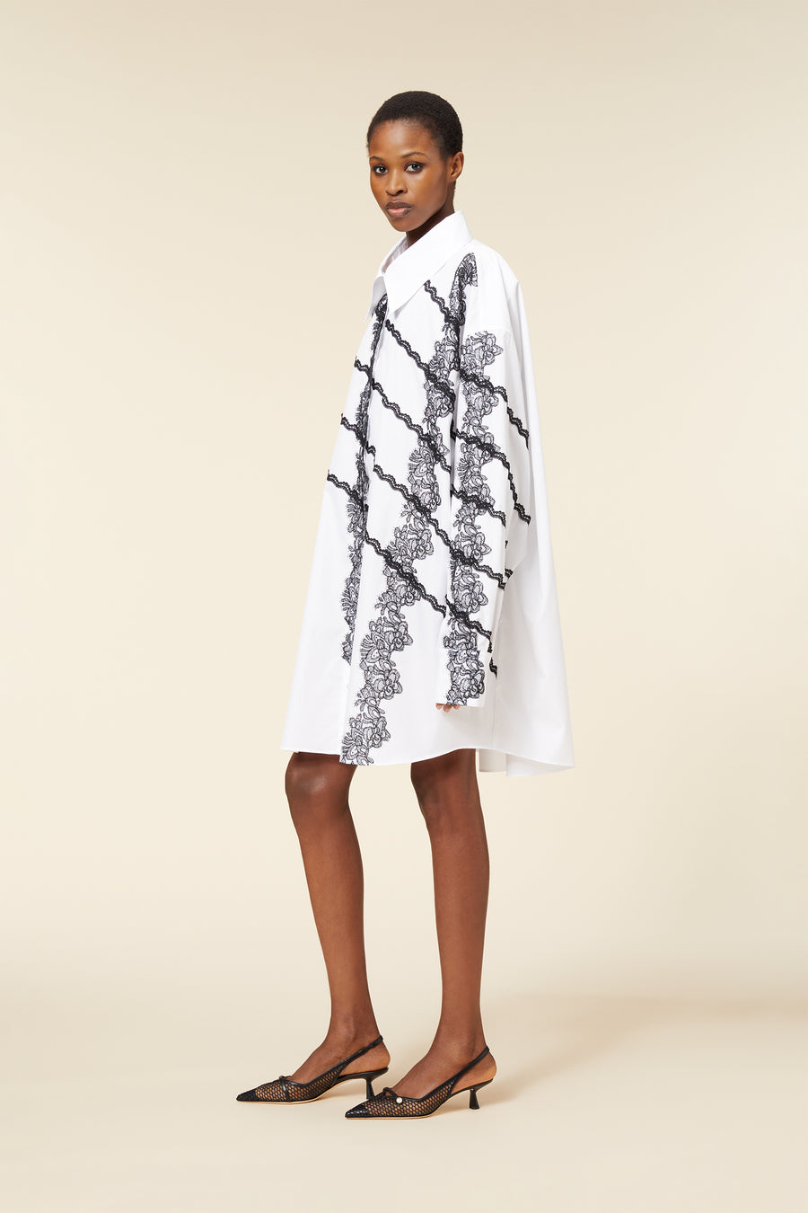 Elegant shirt dress featuring intricate black lace patterns on a crisp white background, paired with stylish black mesh pumps.