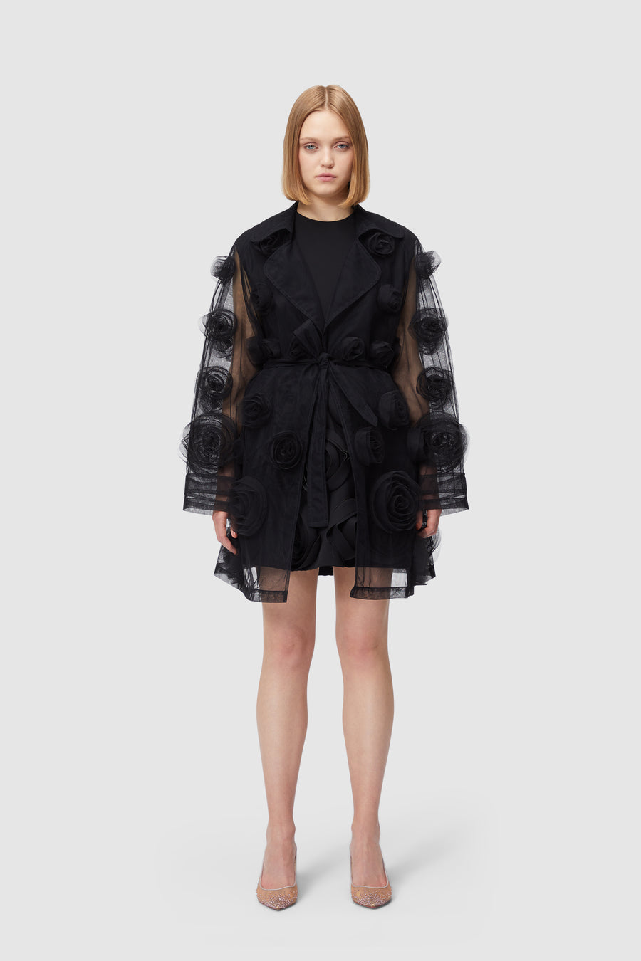 Black sheer tulle coat adorned with intricate floral appliqué rosettes, featuring wide lapels and a belted waist.