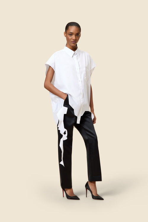 Model wearing a white oversized short-sleeve shirt and black pants with white abstract design, styled with black heels.