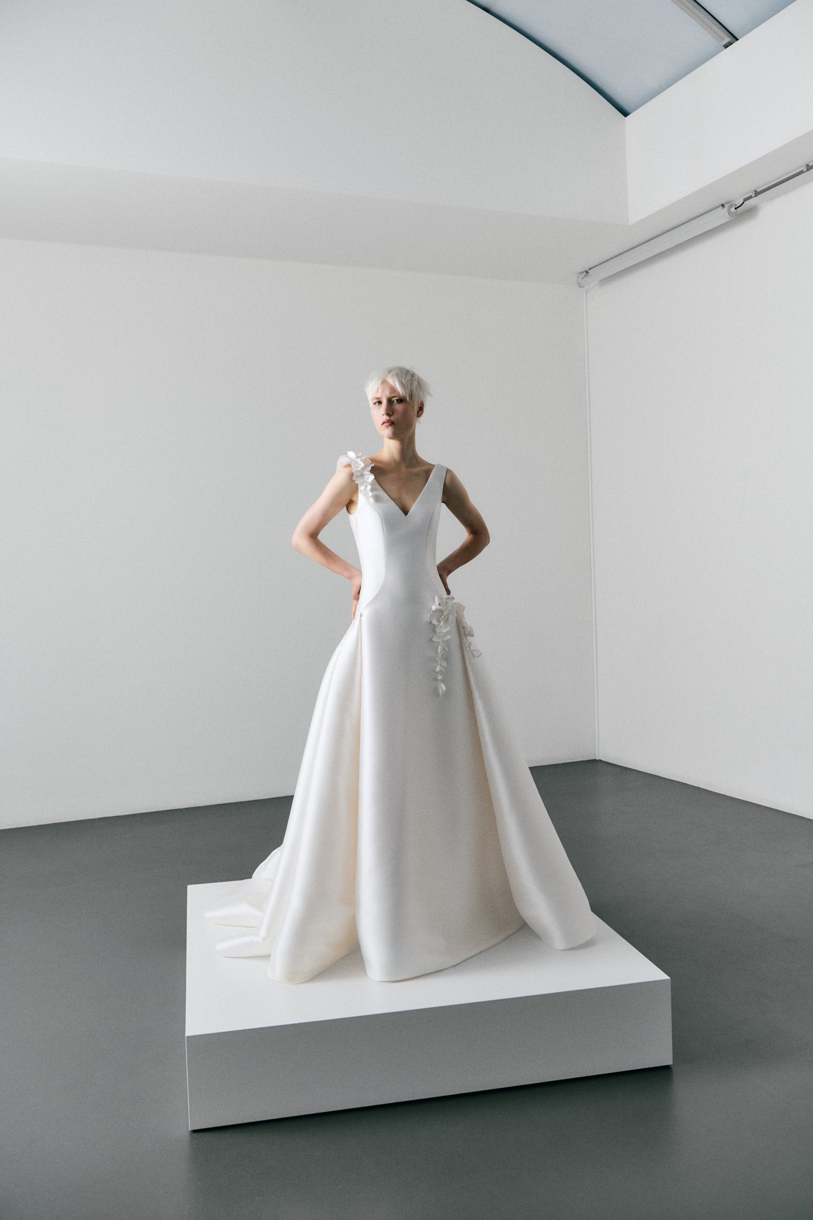 White wedding dress on a mannequin in a minimalistic room with white walls and gray floor.