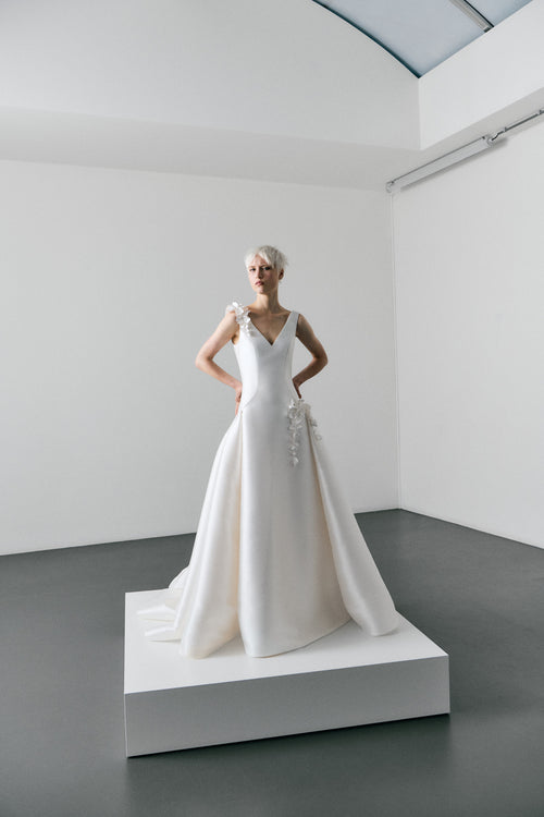 White wedding dress on a mannequin in a minimalistic room with white walls and gray floor.