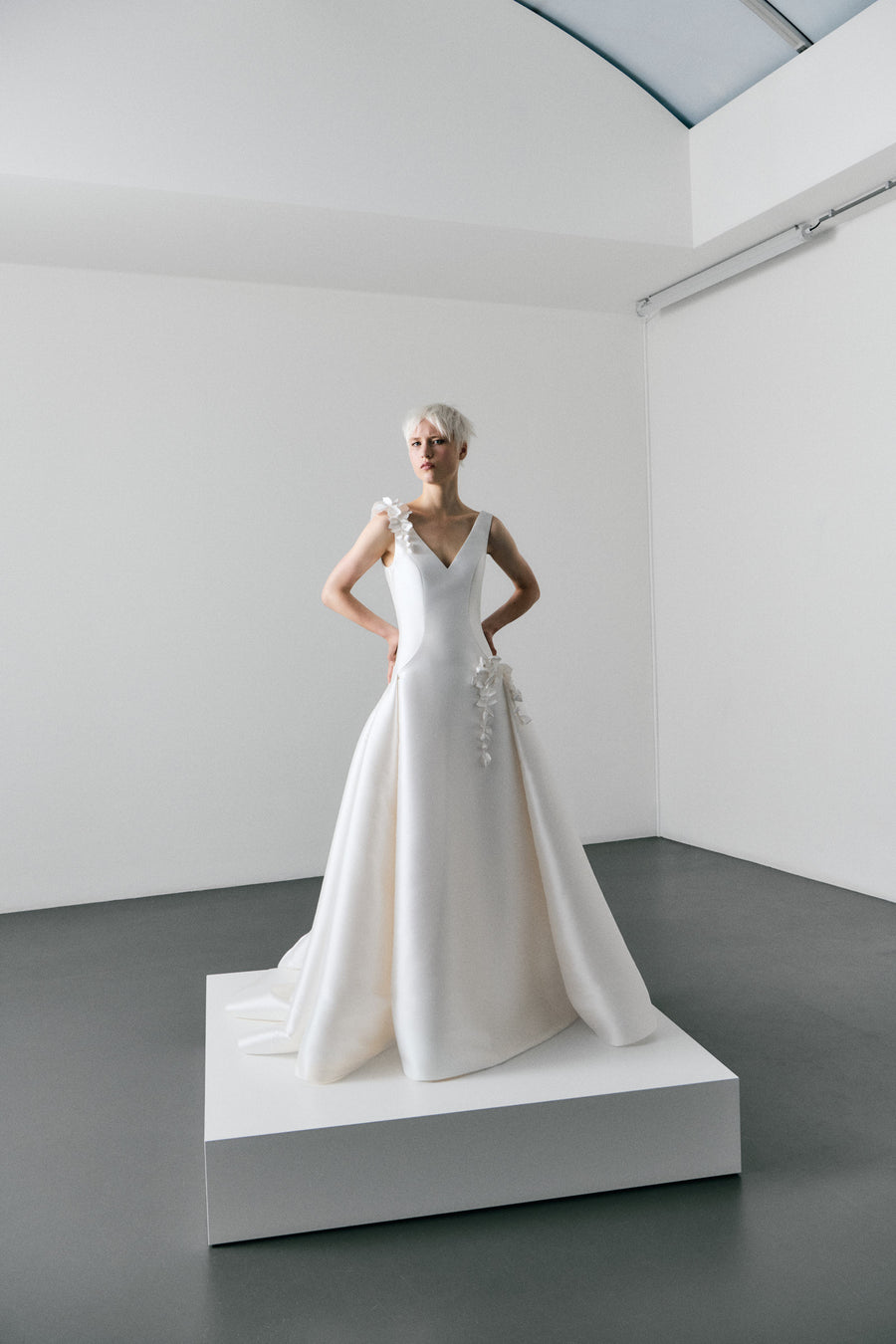 White wedding dress on a mannequin in a minimalistic room with white walls and gray floor.