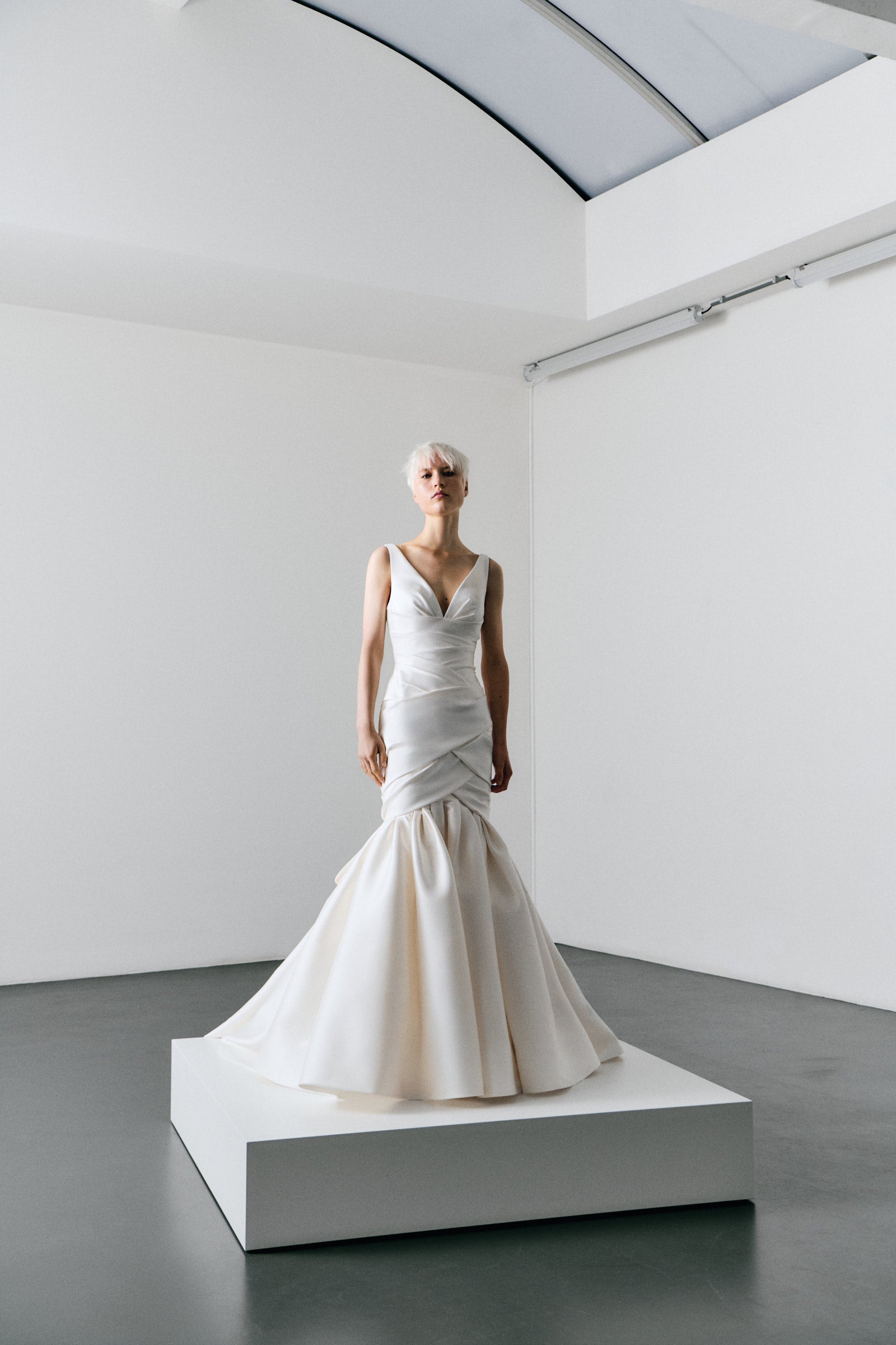 White wedding dress on a mannequin in a minimalistic room with white walls and gray floor.
