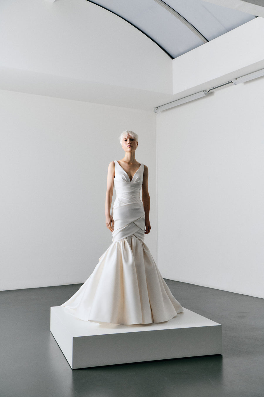 White wedding dress on a mannequin in a minimalistic room with white walls and gray floor.