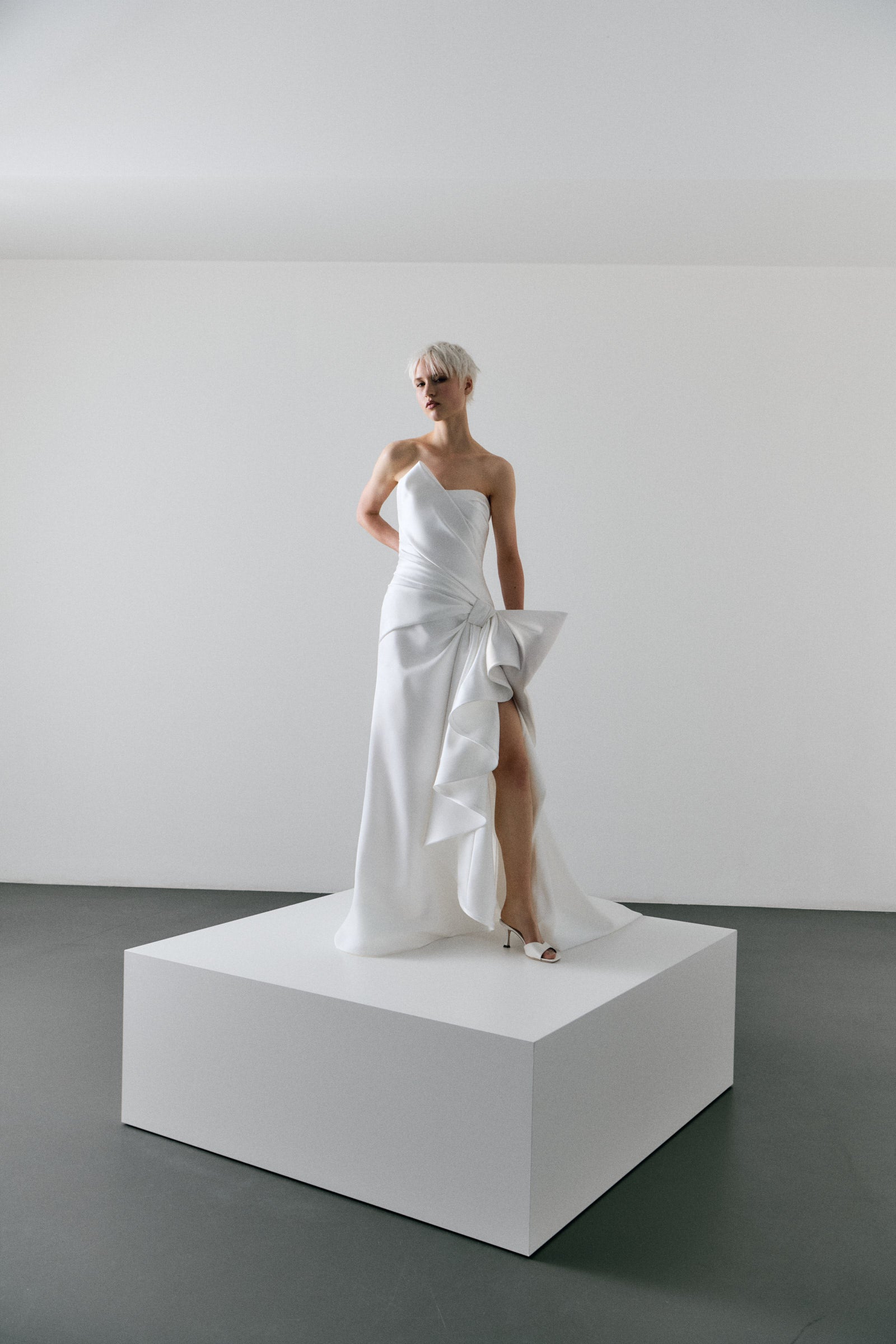 Woman in a white strapless gown standing on a white platform against a plain background