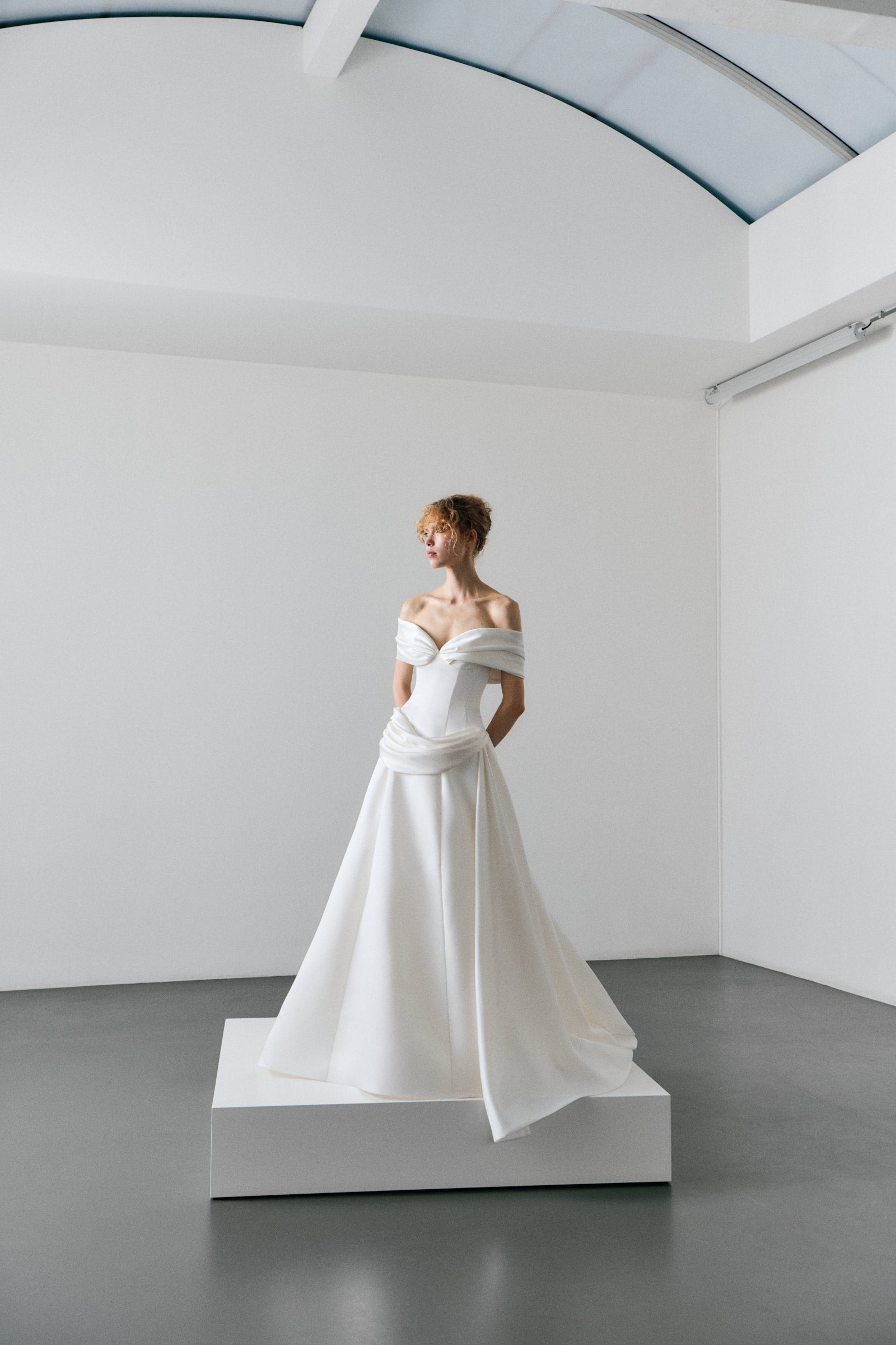 White wedding dress on a mannequin in a minimalistic room with white walls and gray floor.