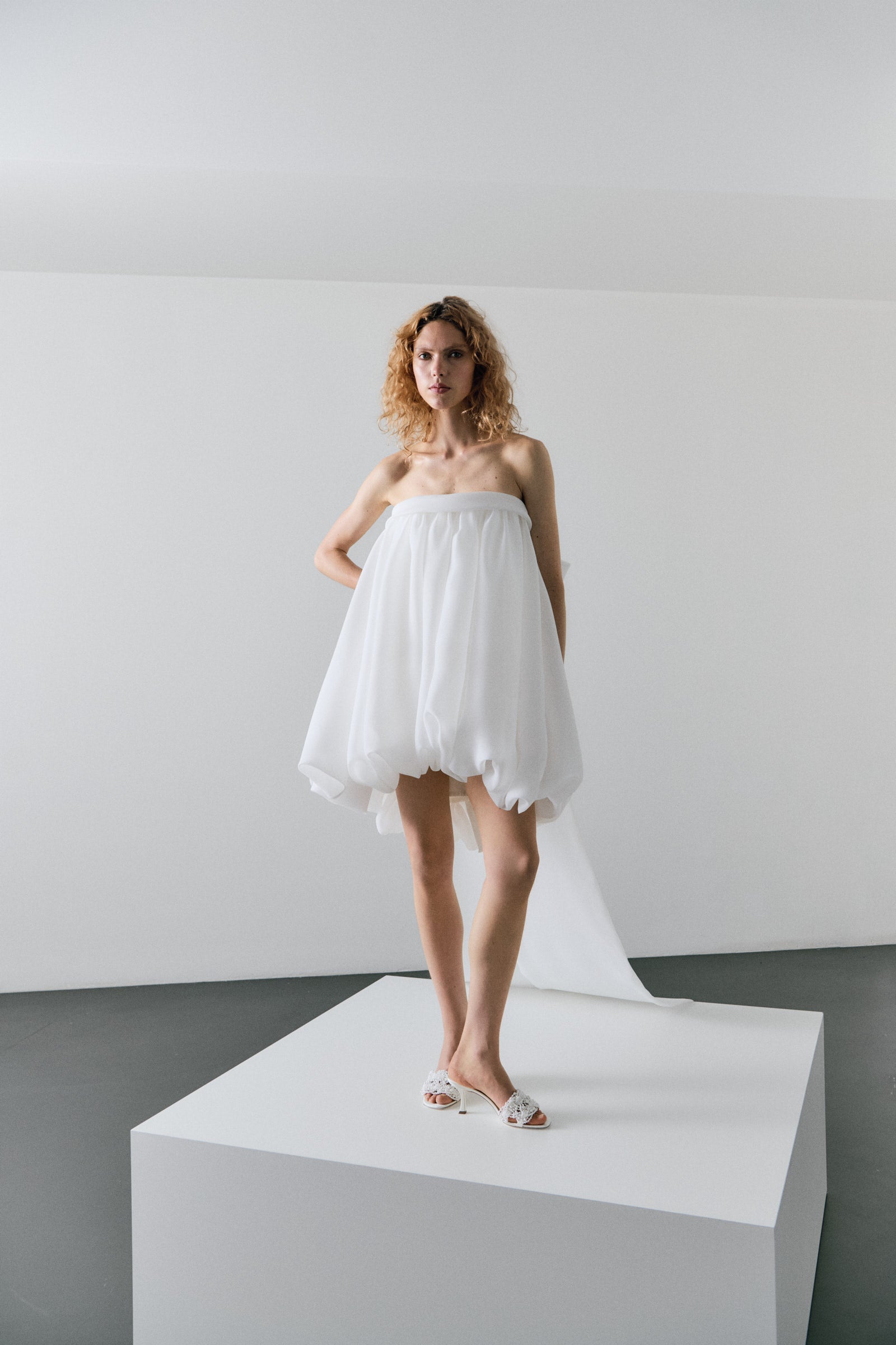 Woman wearing a white strapless dress on a white platform with a plain background