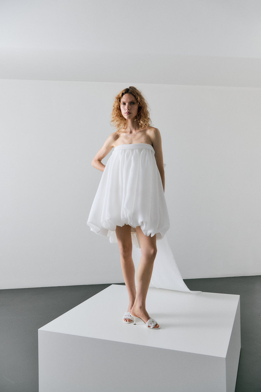 Woman wearing a white strapless dress on a white platform with a plain background