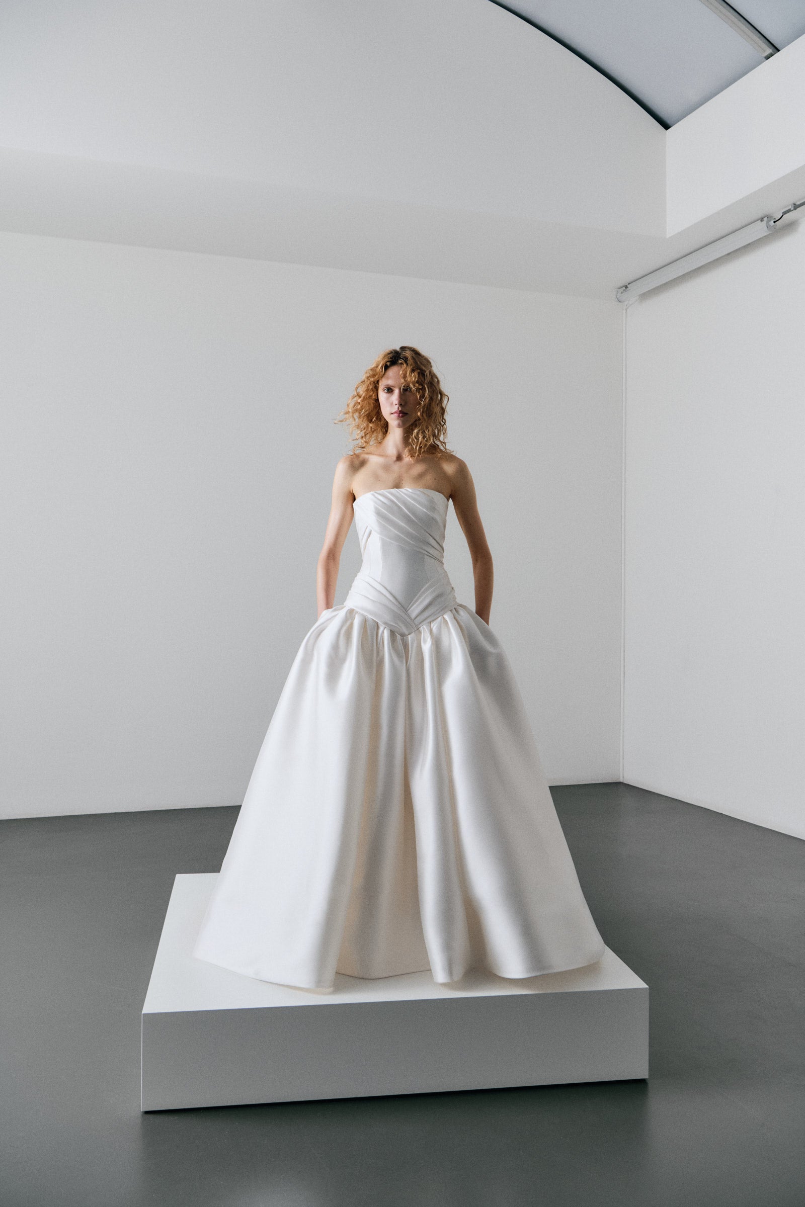 Woman wearing a strapless white wedding dress in a minimalistic room.