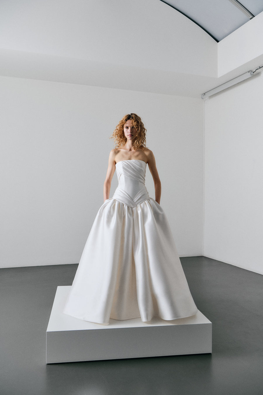 Woman wearing a strapless white wedding dress in a minimalistic room.