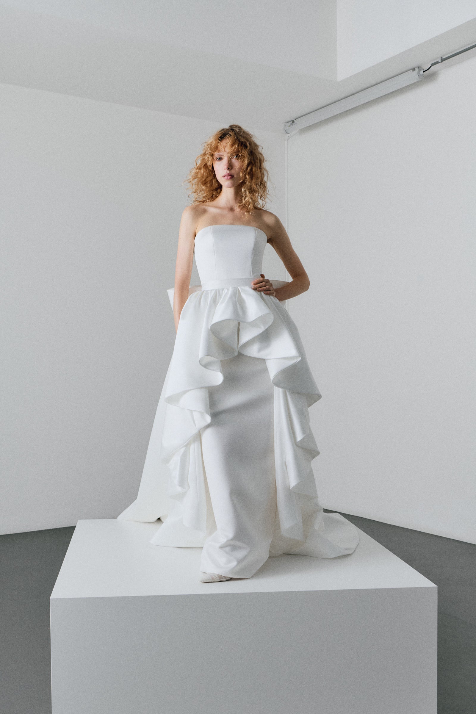 Woman wearing a white strapless gown with ruffled layers on a white platform.