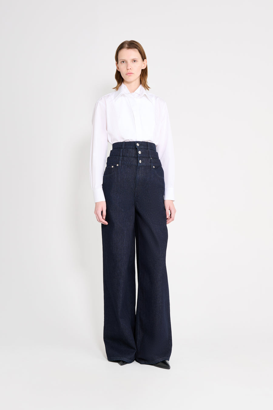 Woman wearing a white blouse and dark blue high-waisted pants on a white background