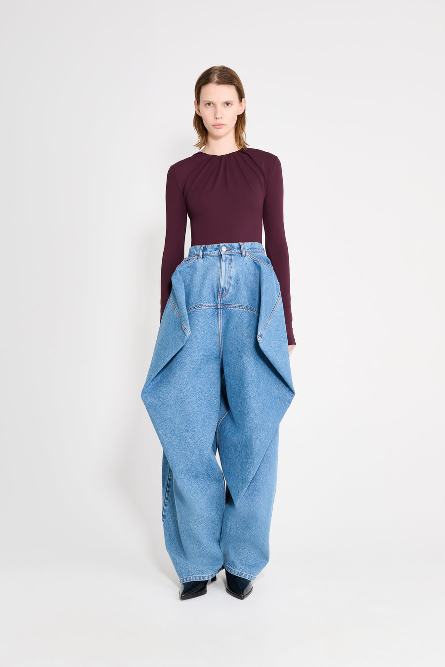 Woman wearing a burgundy top and blue jeans on a white background