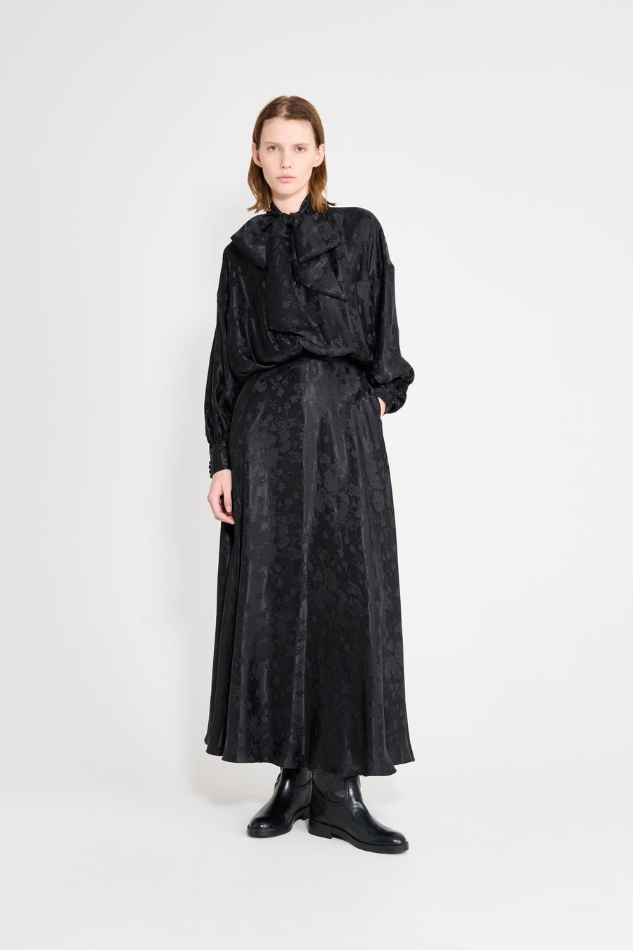 Person wearing a black outfit with a patterned skirt on a white background